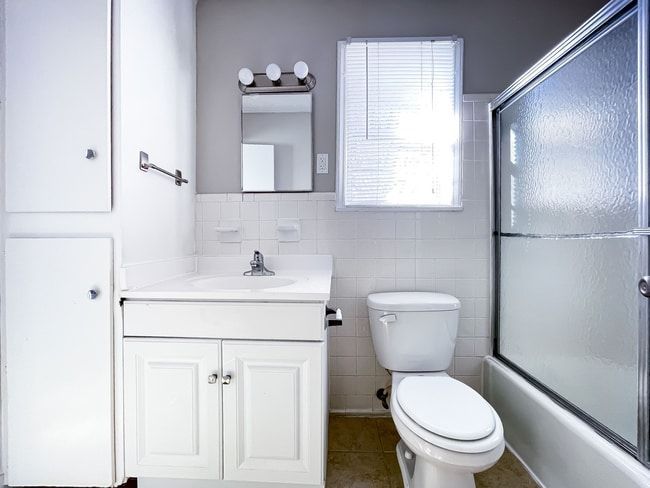 White bathroom with a vanity, toilet, shower, and window.