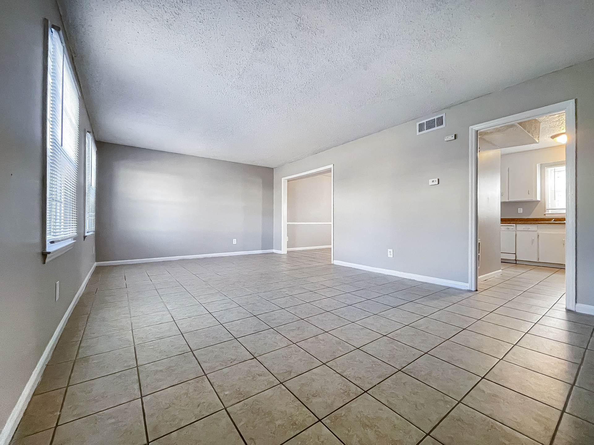 Living room with tiled floor and neutral gray walls, open to the kitchen.