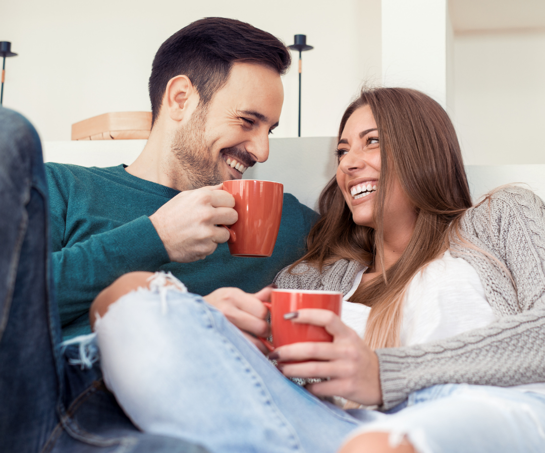 Man and woman smiling, holding red mugs, looking at each other.