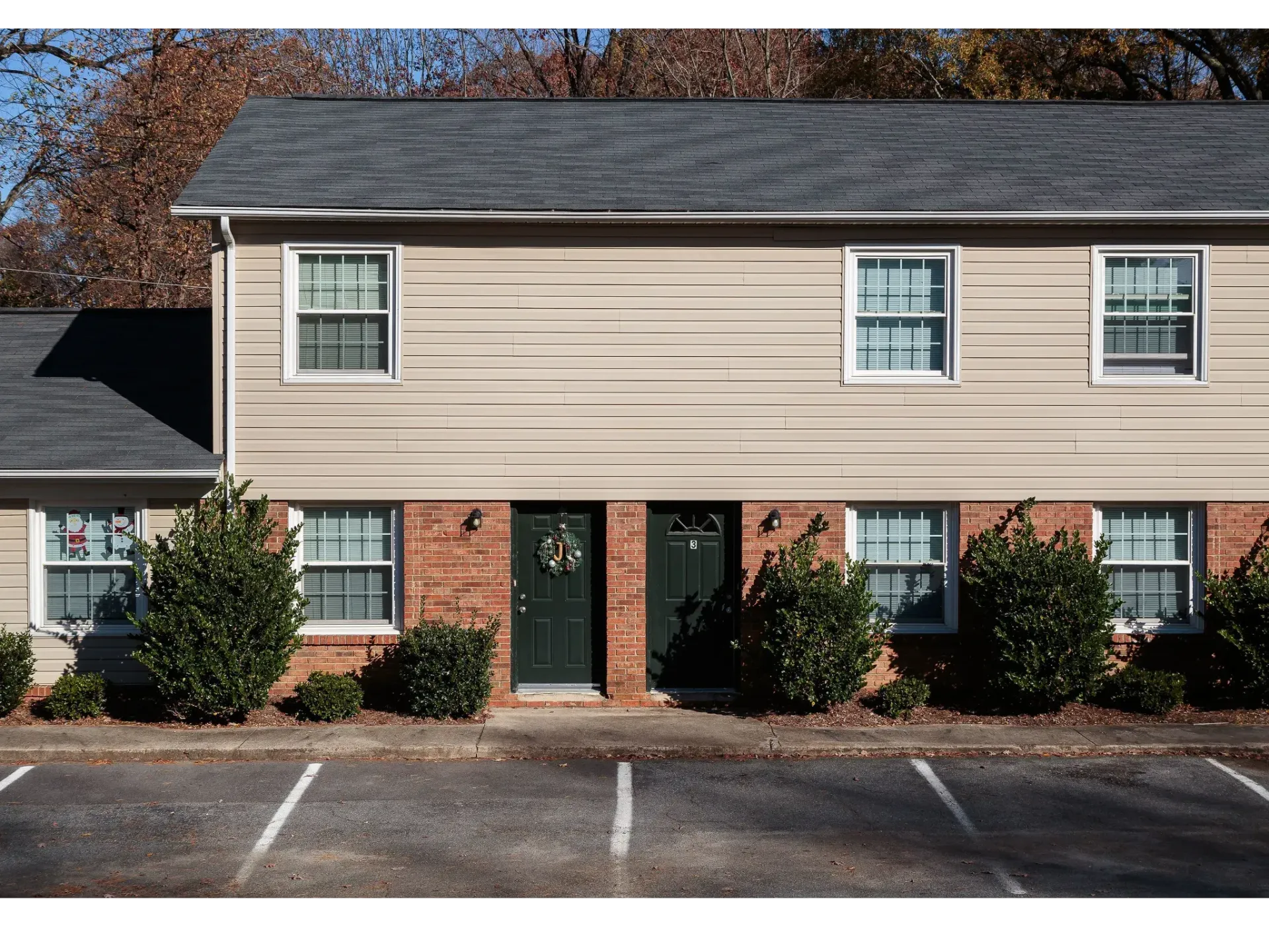 Exterior view of a two-story beige apartment building with brick base and front parking.