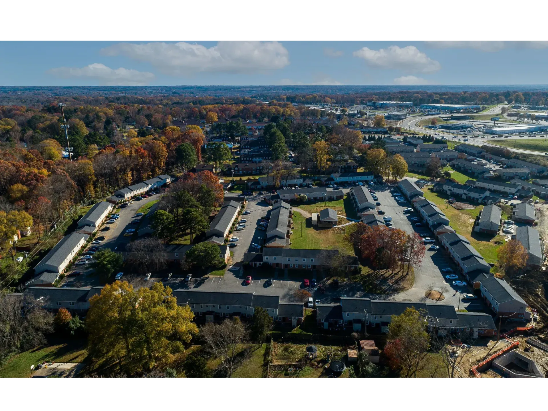 Aerial view of a multi-building apartment community with lots of parking and autumn trees.