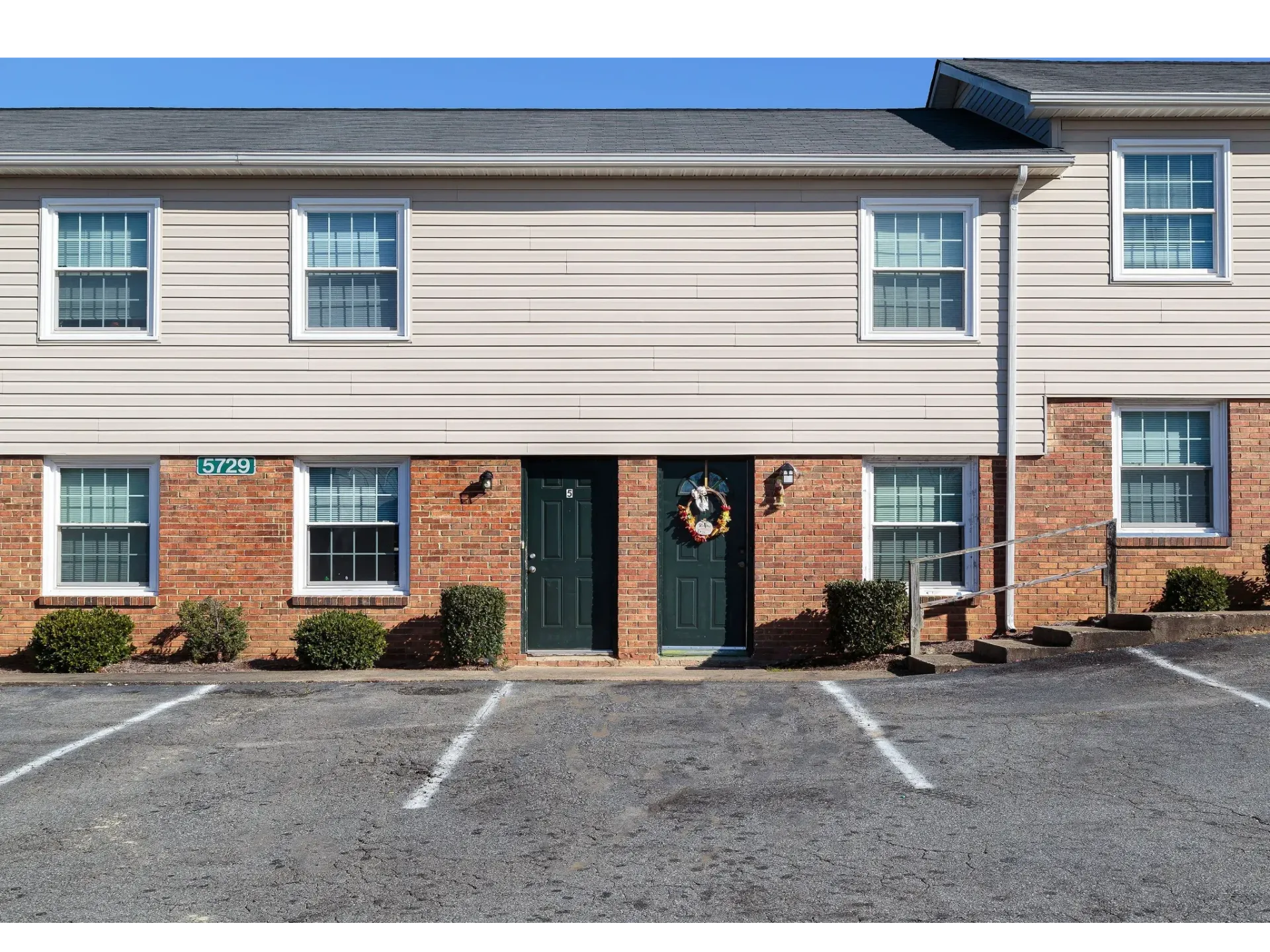 Exterior view of a two-door entry apartment building with a parking lot in front.