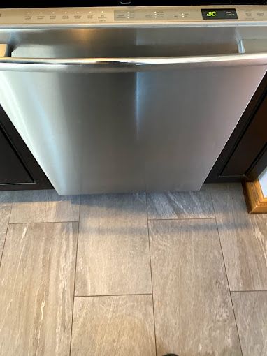 A stainless steel dishwasher is sitting on a tiled floor in a kitchen.