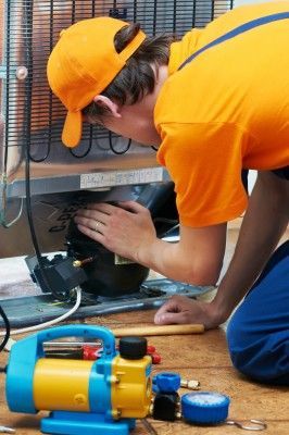 A man in an orange shirt is working on a refrigerator.