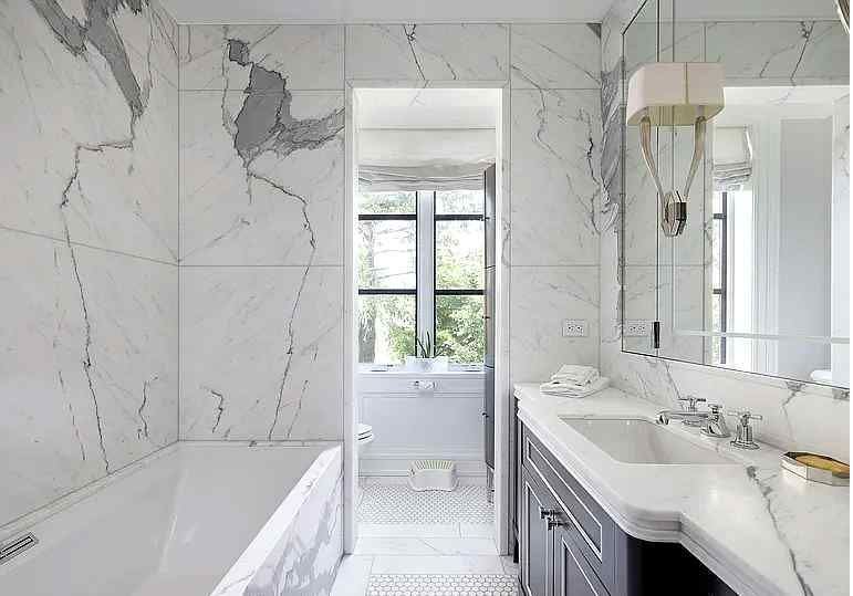 A bathroom with marble tiles , a tub , sink and mirror.