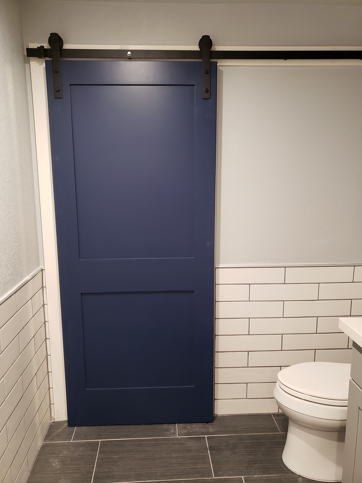 Blue barn door in a bathroom with white tile and a toilet.