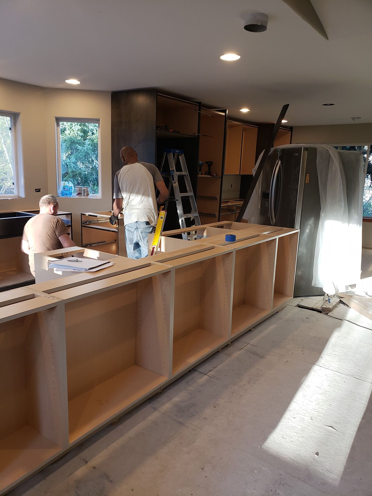 Construction of a kitchen island: men building cabinetry in a room with unfinished walls and cabinets.