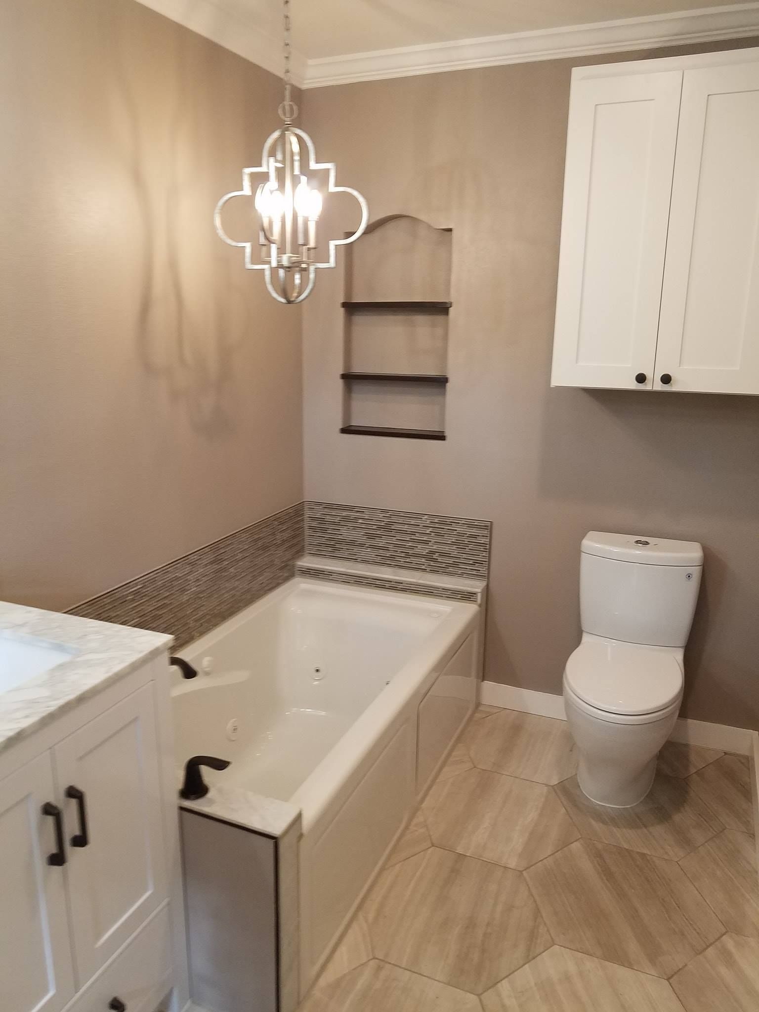 Bathroom with white tub, toilet, and cabinetry. Beige walls and floors. Decorative light fixture.