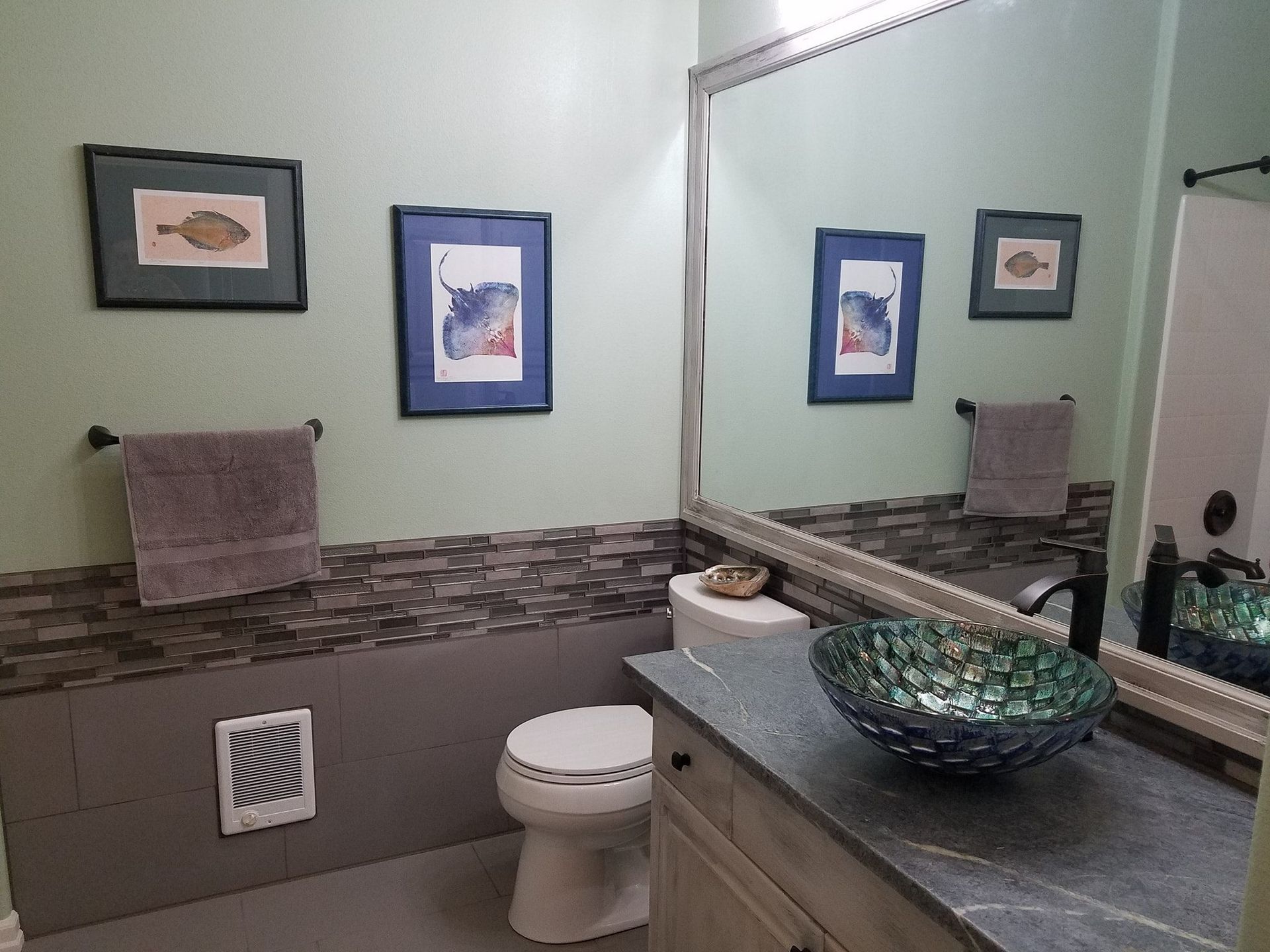 Bathroom with green walls, artwork, decorative sink, toilet, mirror, and towel rack.