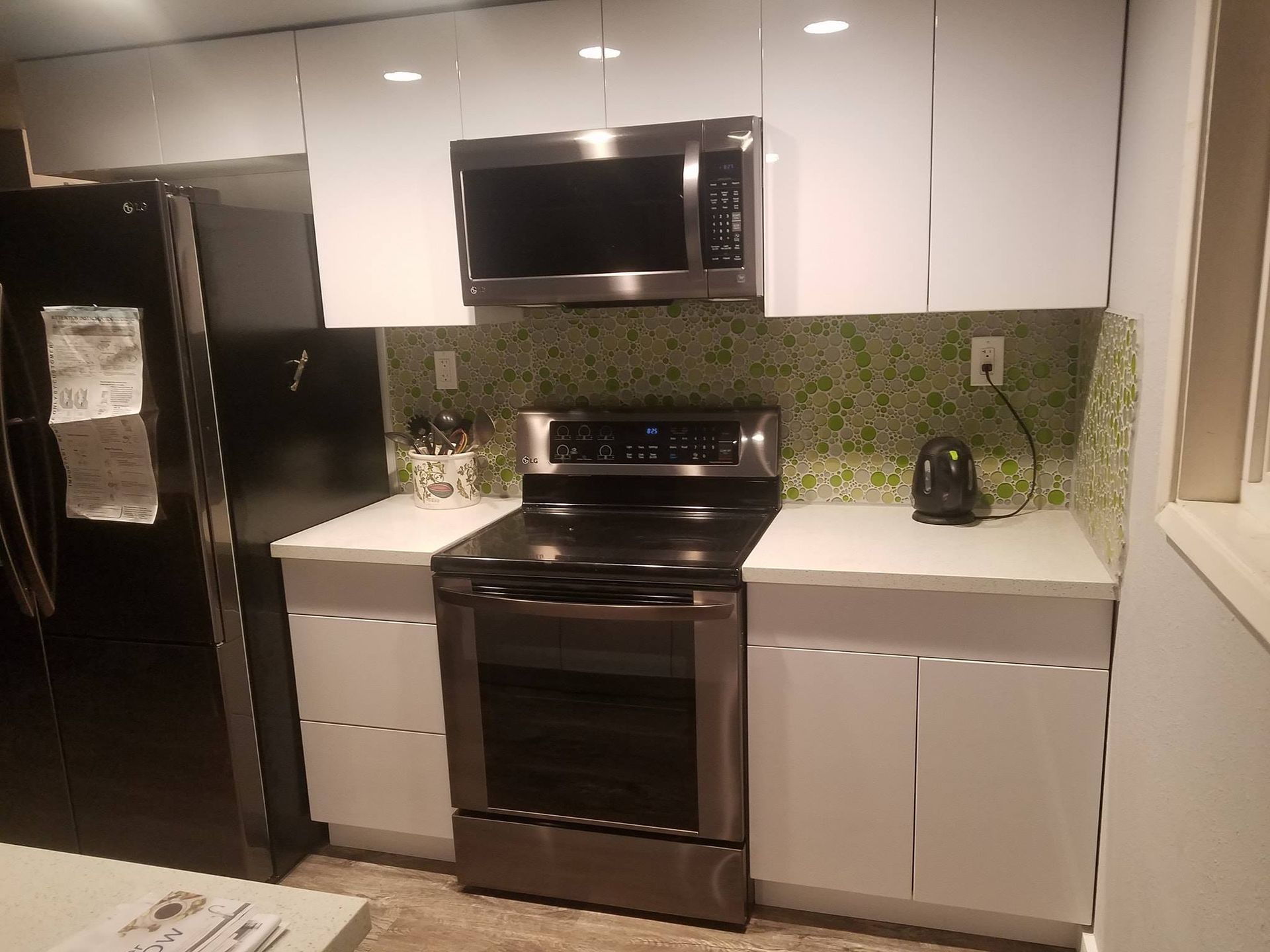 Modern kitchen with white cabinets, black fridge, stainless steel appliances, and green mosaic backsplash.