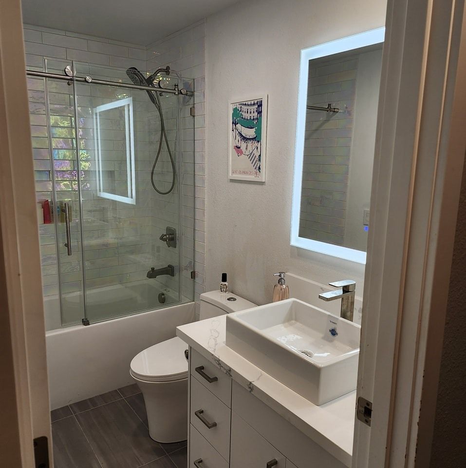 Modern bathroom with a white vanity, toilet, shower, and a lighted mirror.