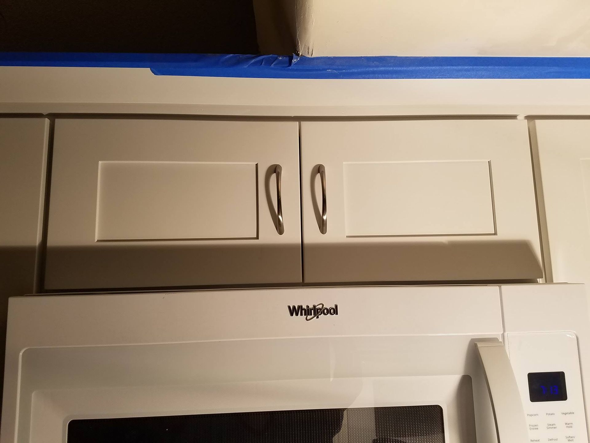 White kitchen cabinets over a microwave. Blue painter's tape above.