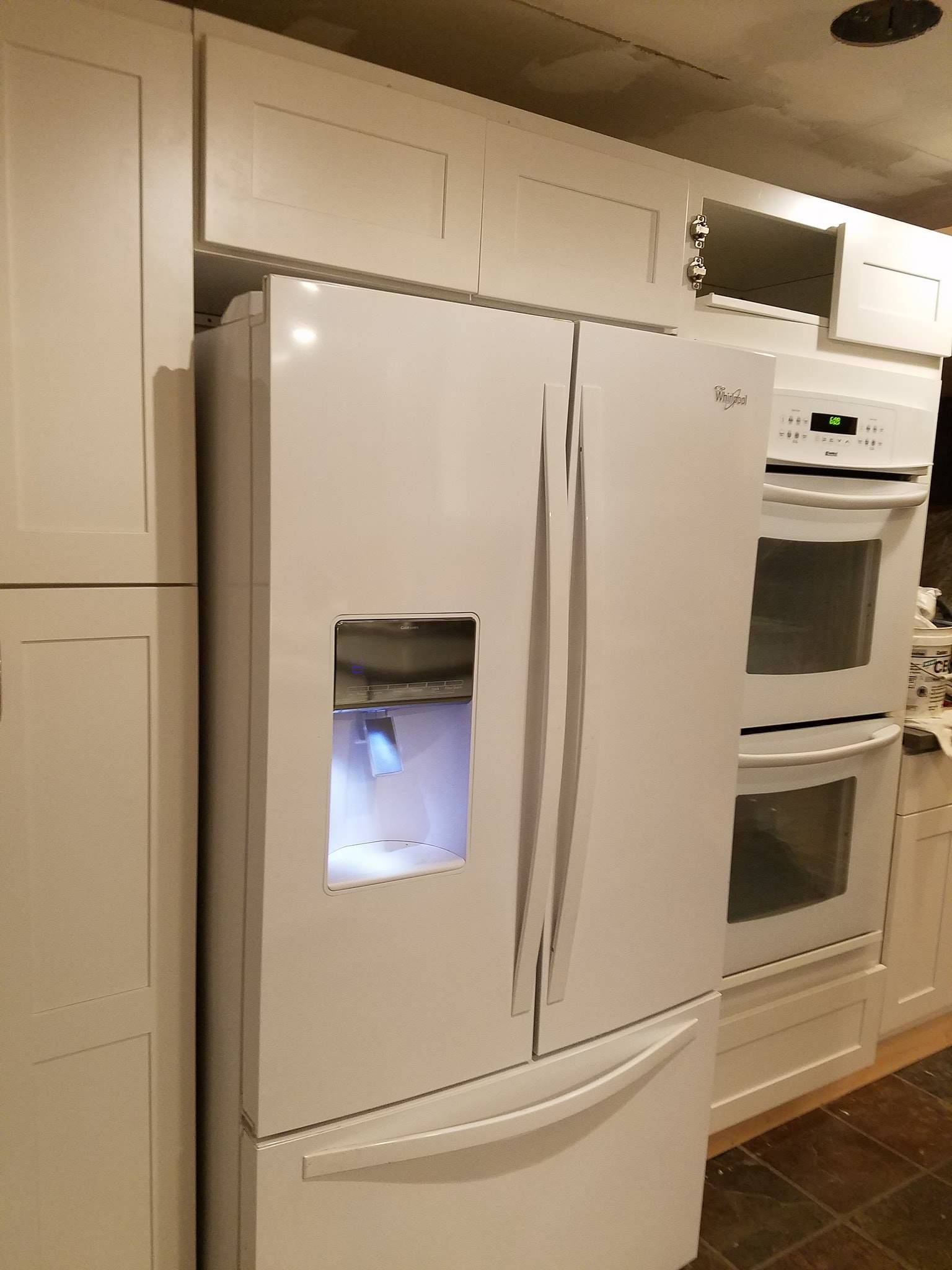 White refrigerator in a kitchen with white cabinets and a double oven.