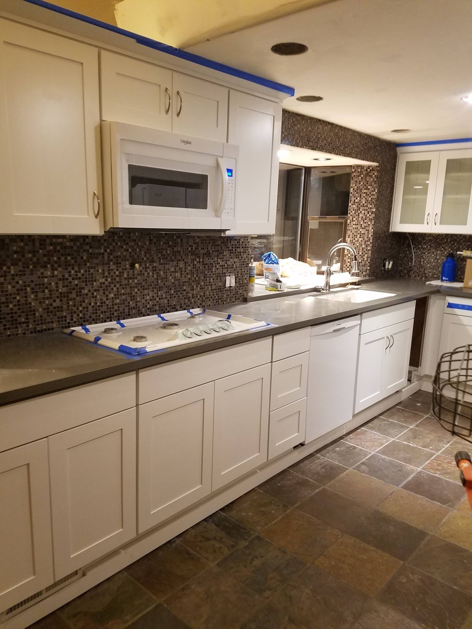 White kitchen cabinets with gray countertops and dark backsplash.