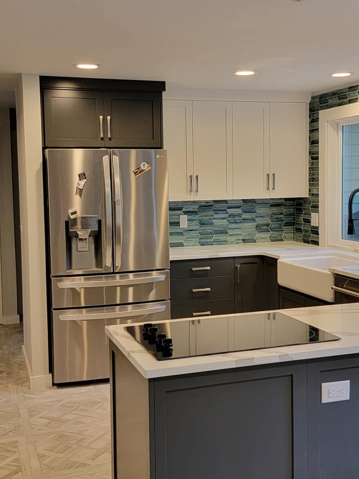 Modern kitchen with stainless steel refrigerator, dark gray and white cabinets, and blue backsplash.