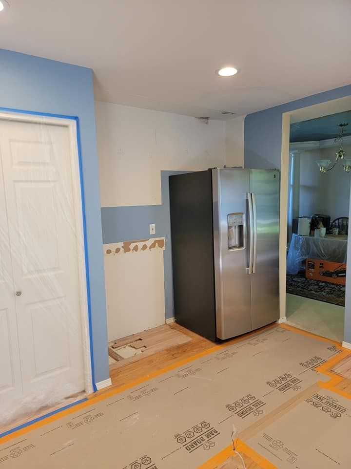 Kitchen interior with blue and white walls, stainless steel refrigerator, and wooden flooring. Door on left.