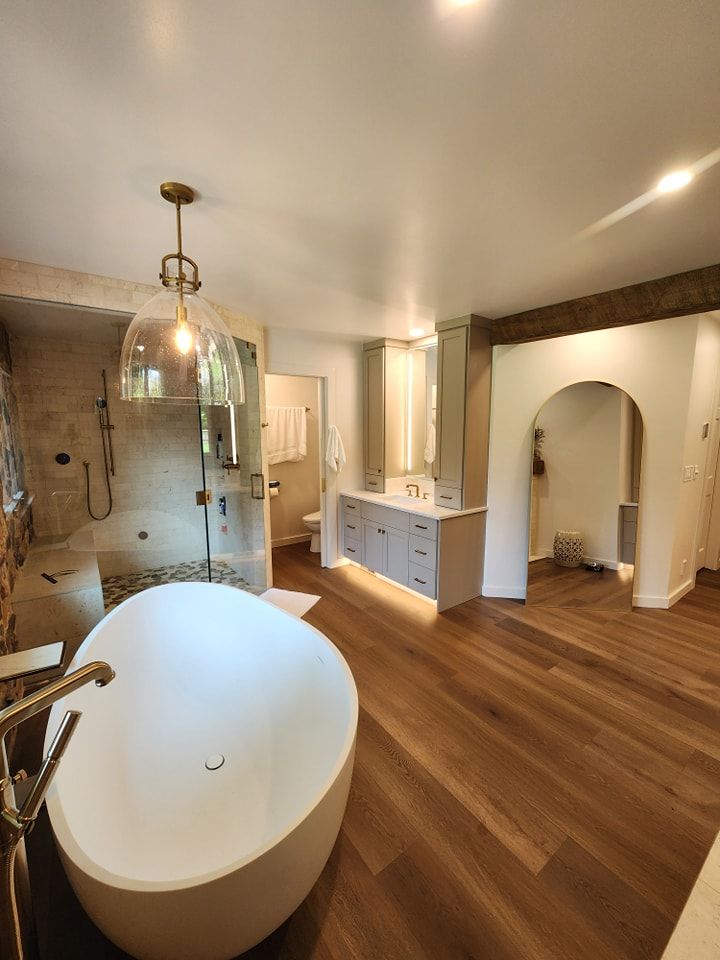 Modern bathroom with white soaking tub, glass shower, and wood flooring.