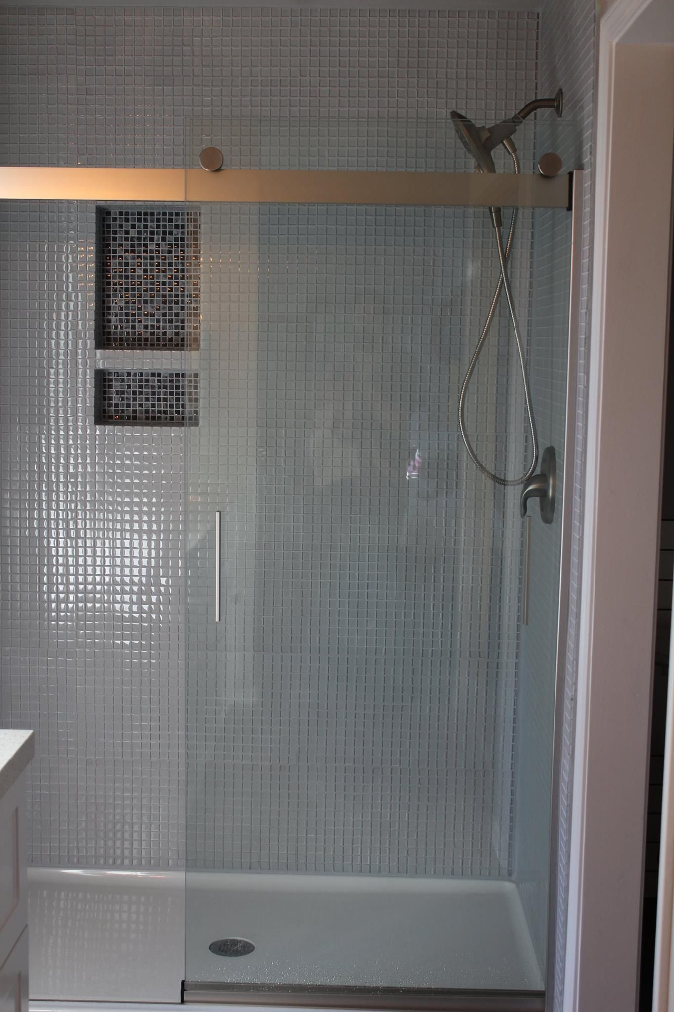 Shower with light blue mosaic tile walls, glass door, and silver fixtures.