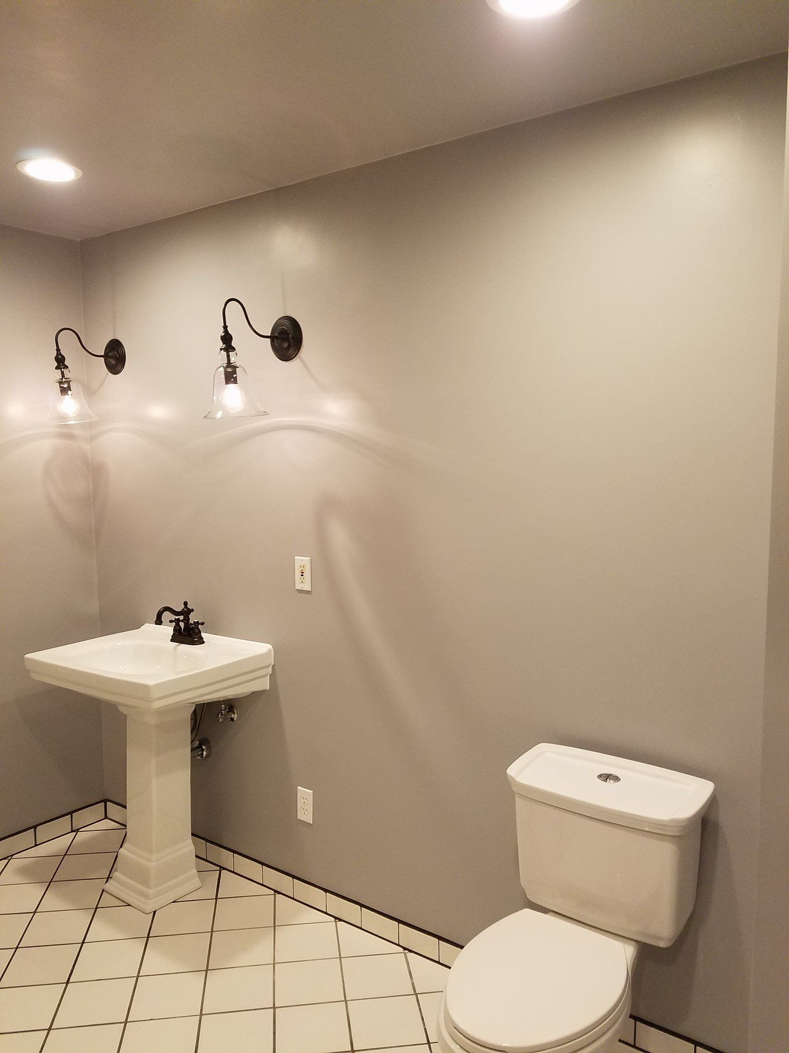 Small bathroom with pedestal sink, toilet, and sconce lighting on gray walls. White and black tile floor.