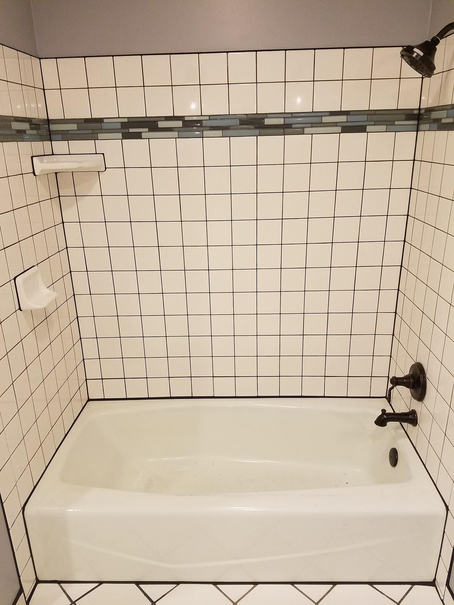 White-tiled bathroom with a bathtub, soap holder, and showerhead. Black accents.