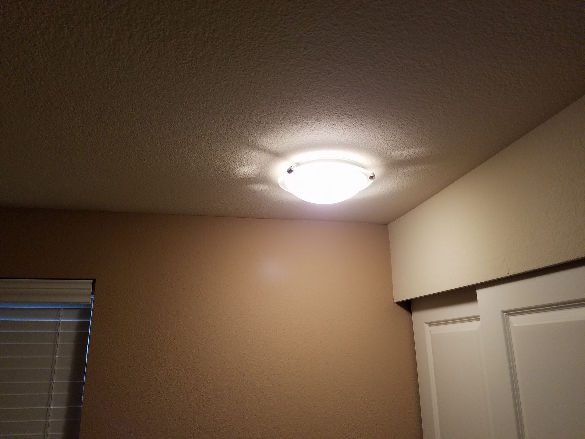Ceiling light illuminates a room with beige walls and a white closet.