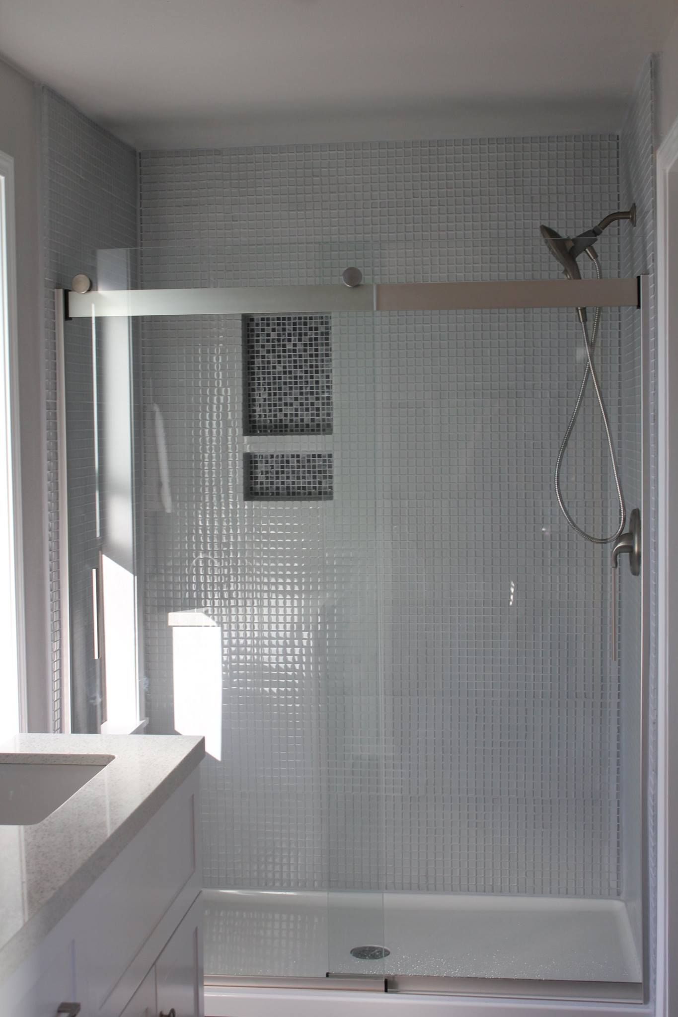 Shower with light gray textured tile, glass door, and showerhead.