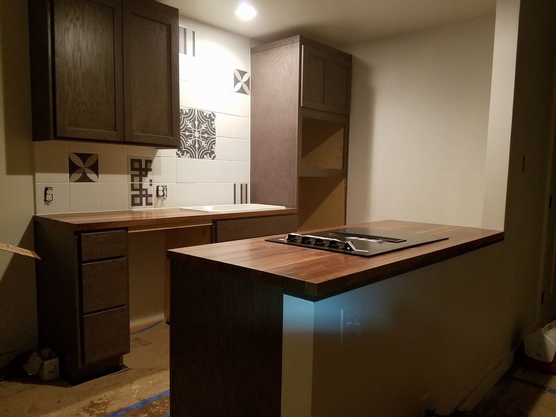 Kitchen renovation: dark cabinets, wood countertops, patterned backsplash, island with cooktop.