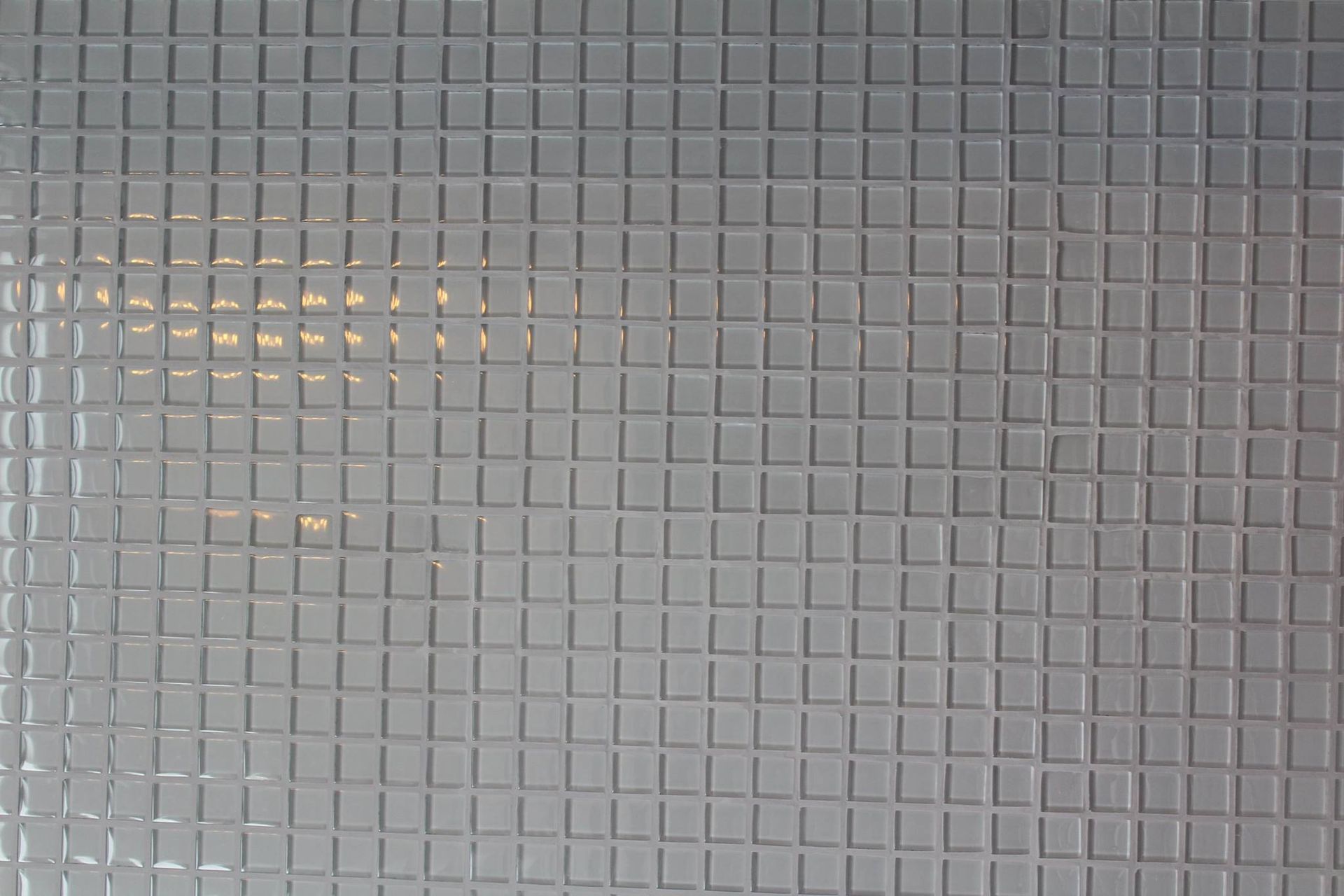Gray, square tile wall with reflections.