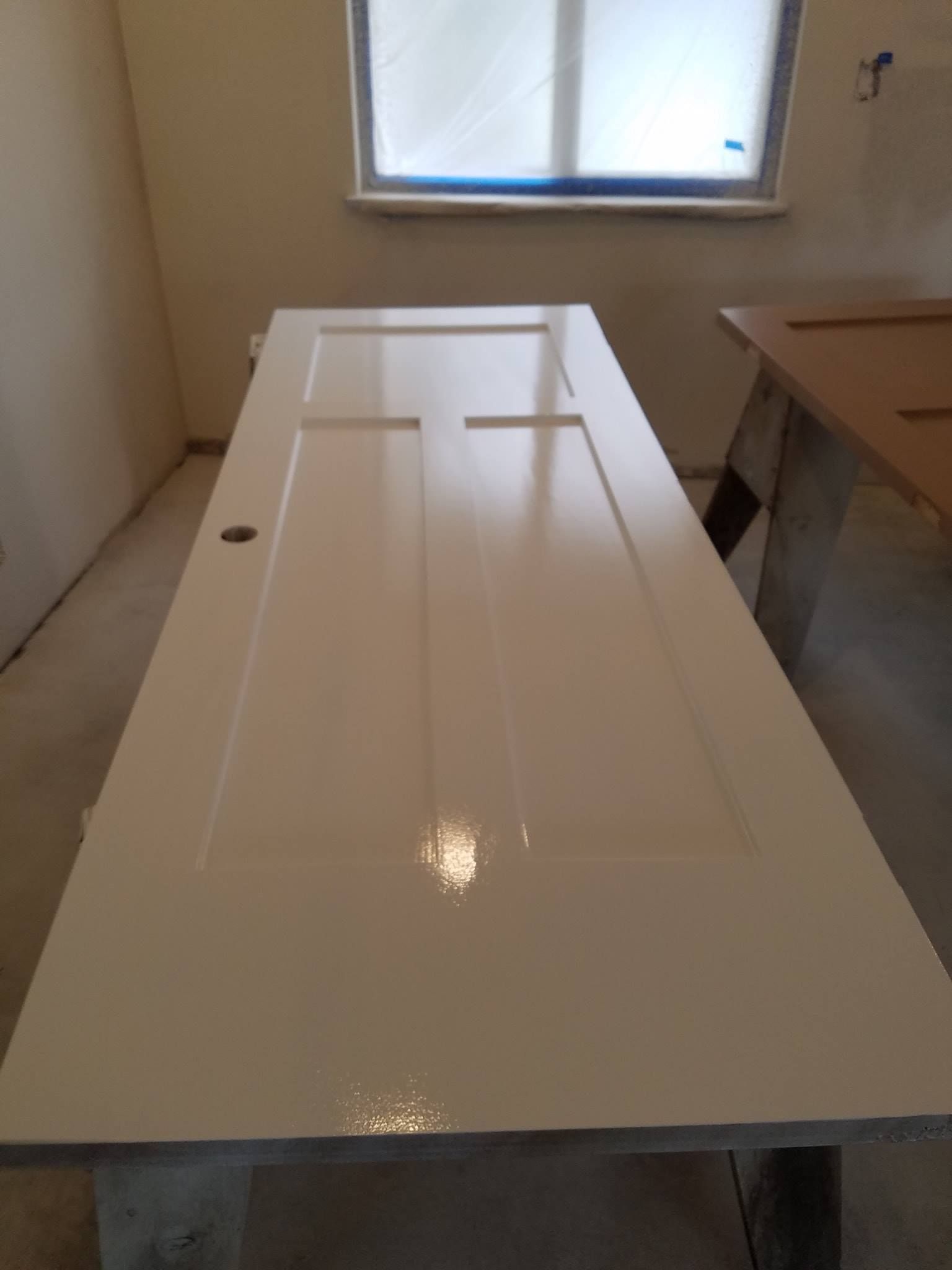 White door, freshly painted and lying horizontally on a table, with a window in the background.