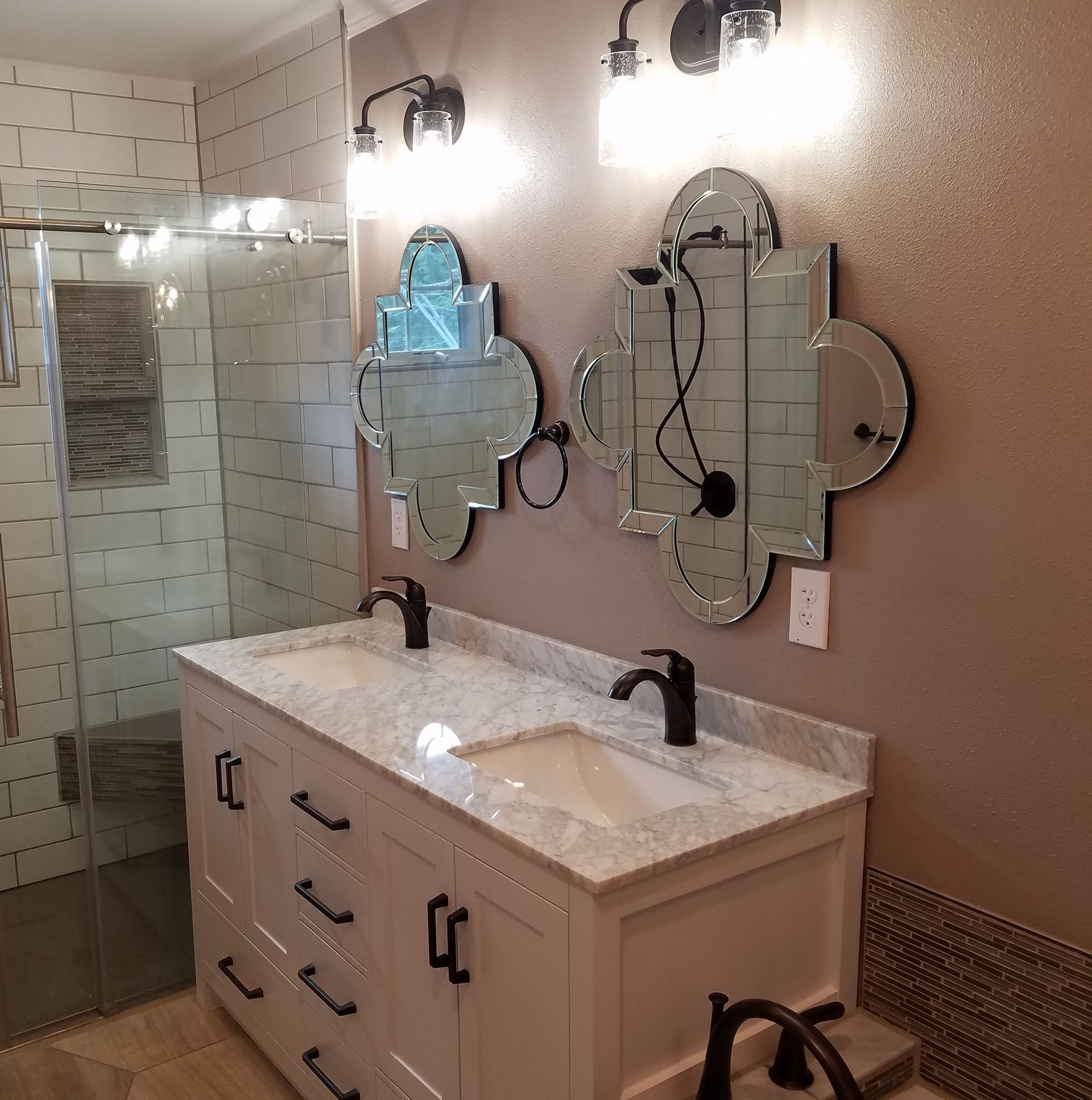 Bathroom with double vanity, decorative mirrors, and a glass shower.
