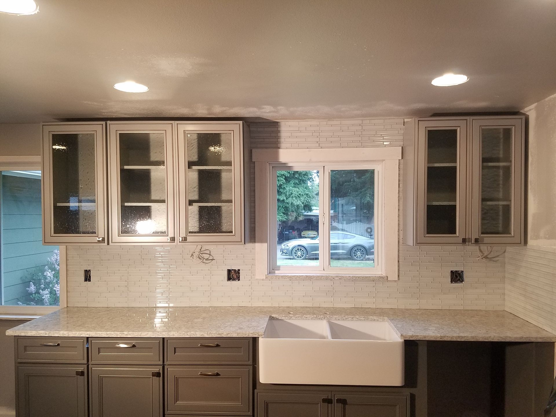 Gray kitchen cabinets with a white tile backsplash, a white sink, and a window.