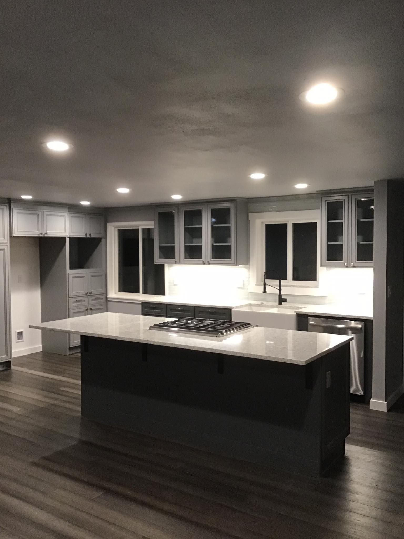 Modern gray kitchen with island, gas stove, glass-front cabinets, and recessed lighting.