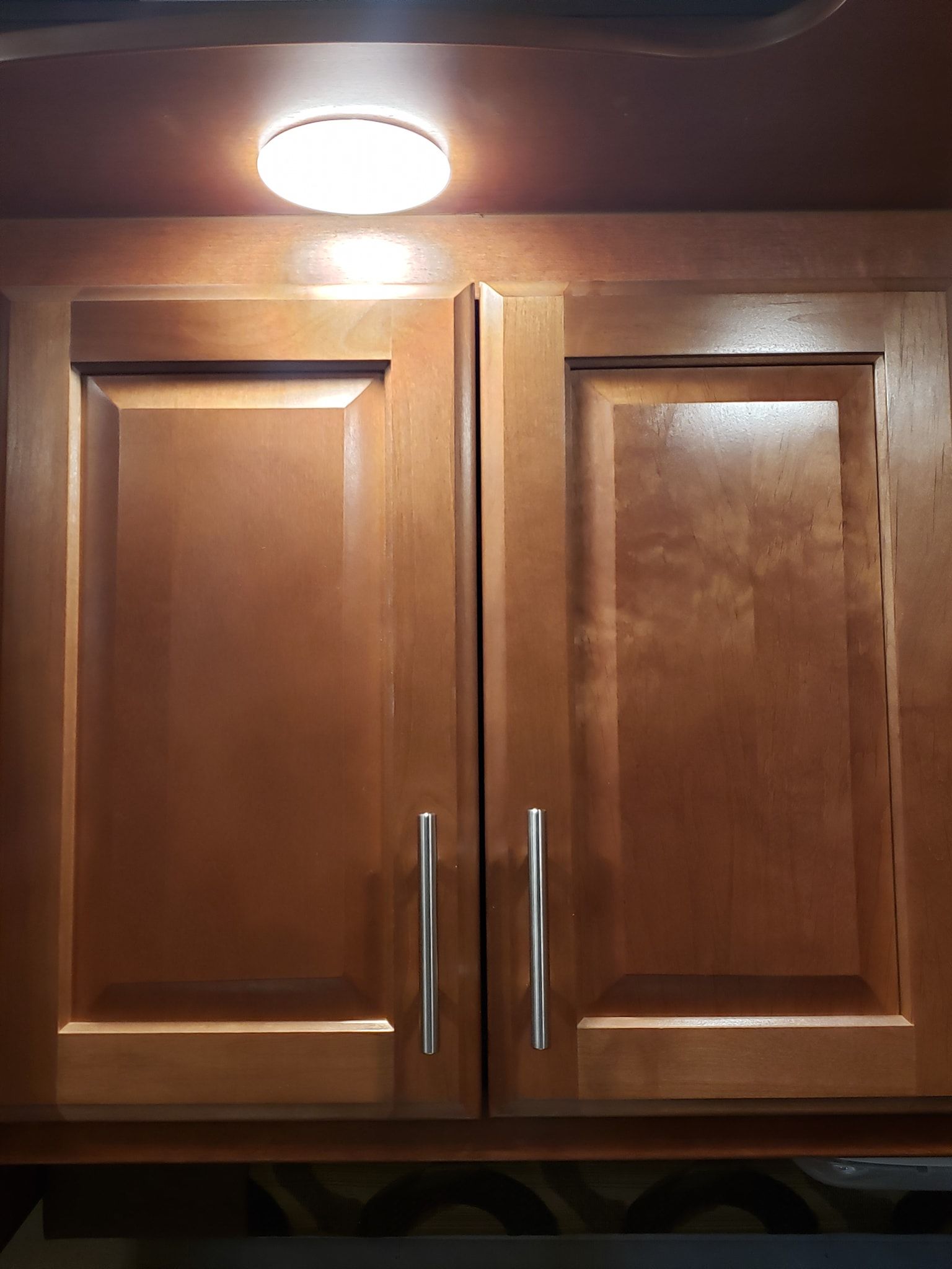 Two wooden kitchen cabinets with silver handles under a bright ceiling light.