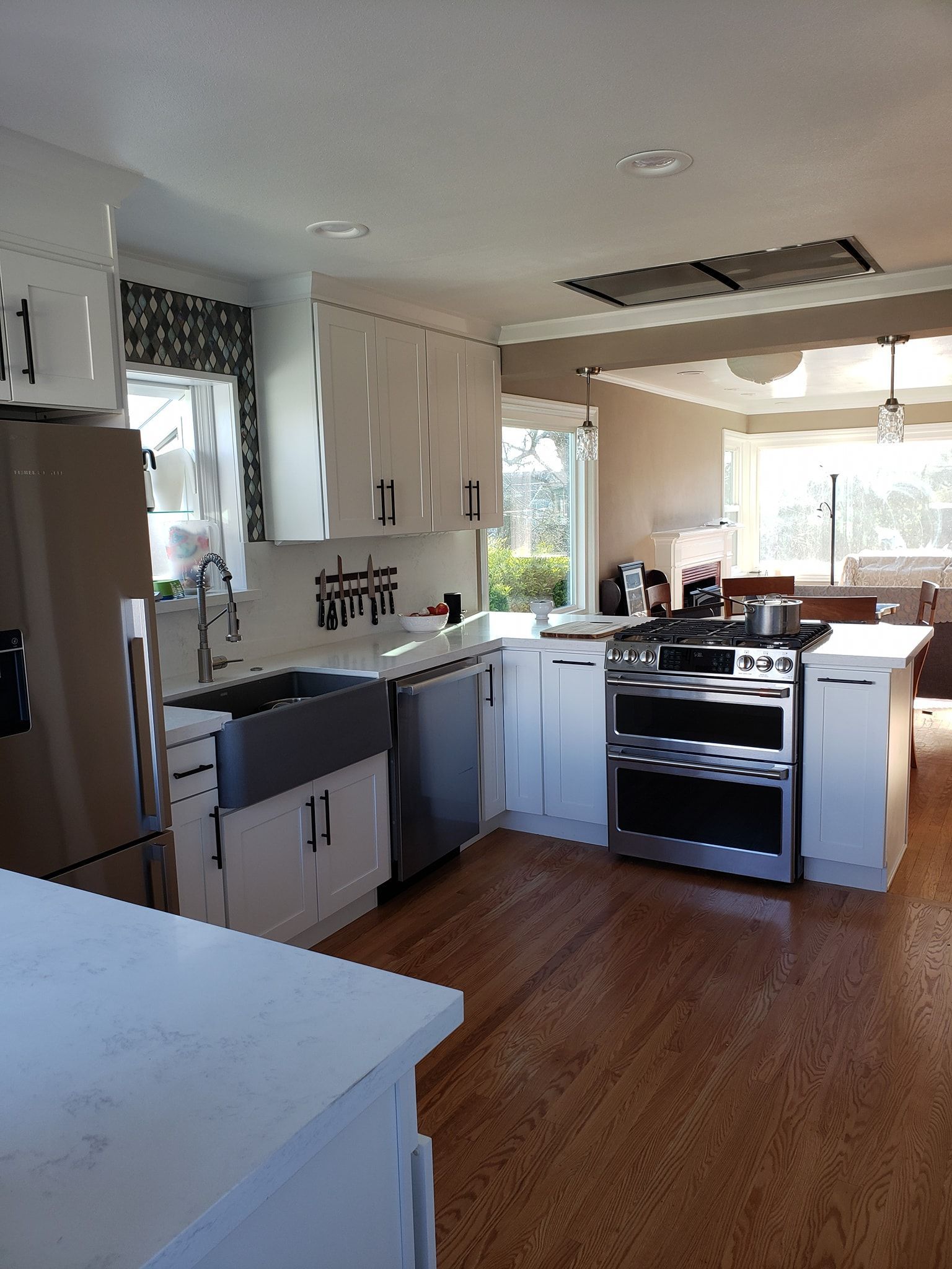 White kitchen with stainless steel appliances, cabinets, and a large range. Cork flooring and light-filled.