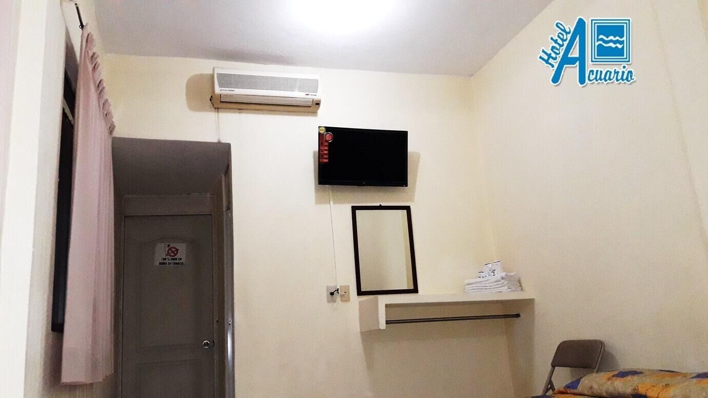 Una habitación de hotel con cama, televisión, espejo y aire acondicionado.