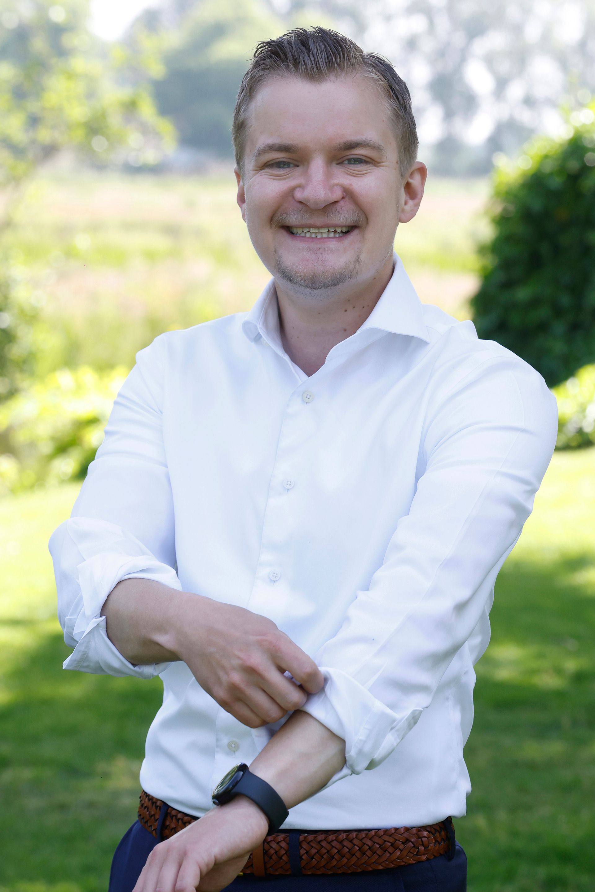Een man in pak en stropdas lacht en heeft zijn armen over elkaar.
