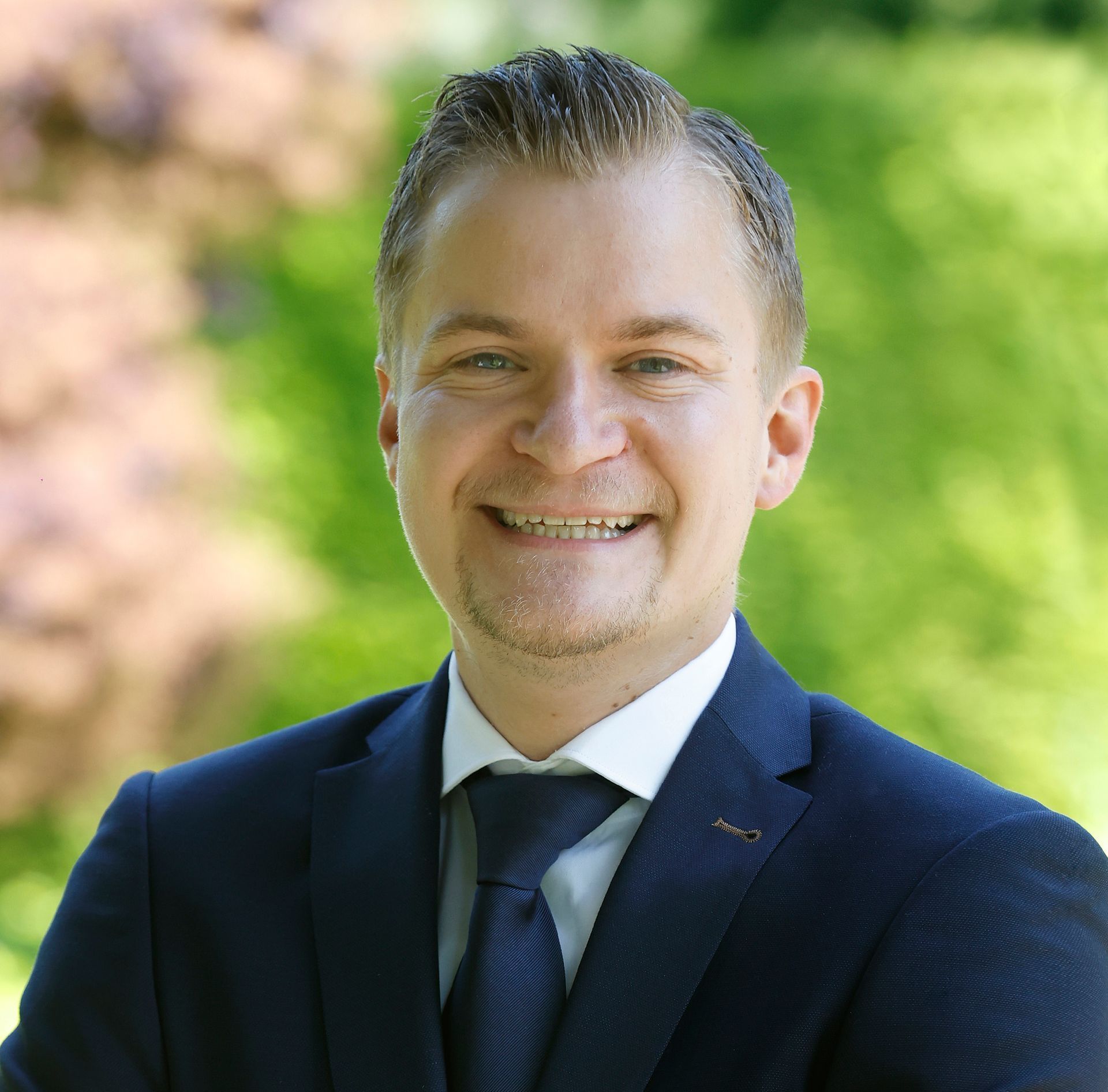 Een man in een wit overhemd lacht en heeft zijn armen over elkaar geslagen.