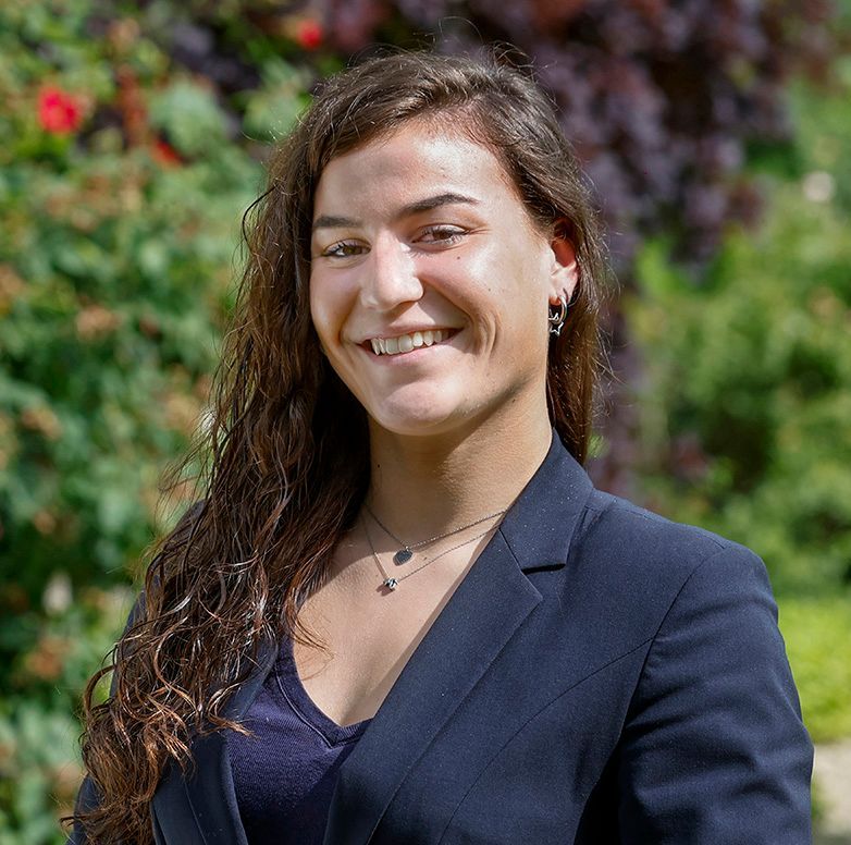 Een vrouw met een bril en oorbellen staat in een veld.