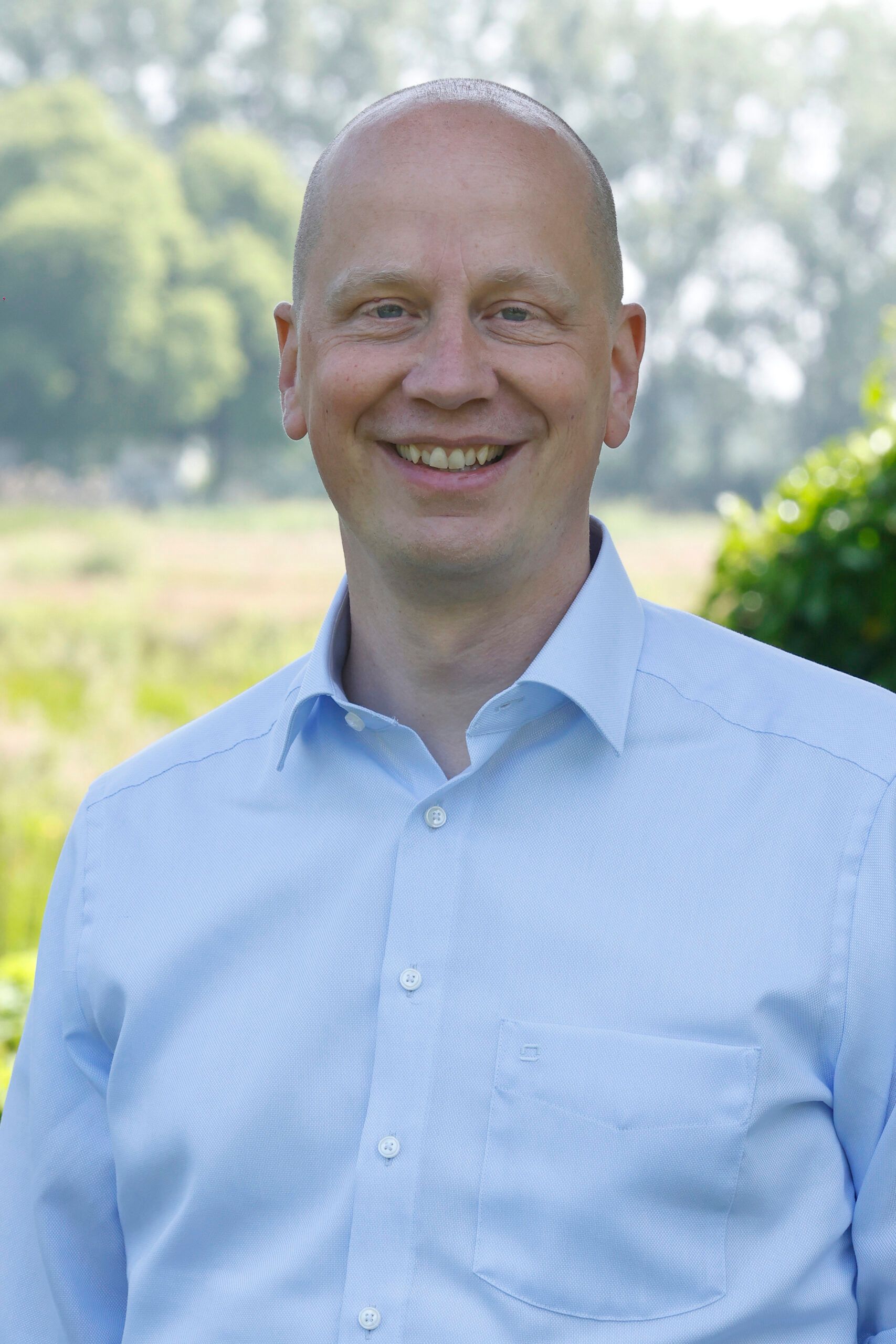 Een man in een blauw shirt lacht naar de camera.