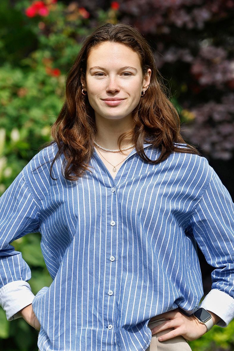 Een vrouw in een blauw-wit gestreept shirt staat met haar handen in haar zij.