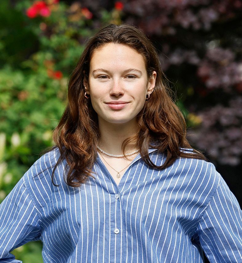 Een vrouw met een bril en oorbellen staat in een veld.