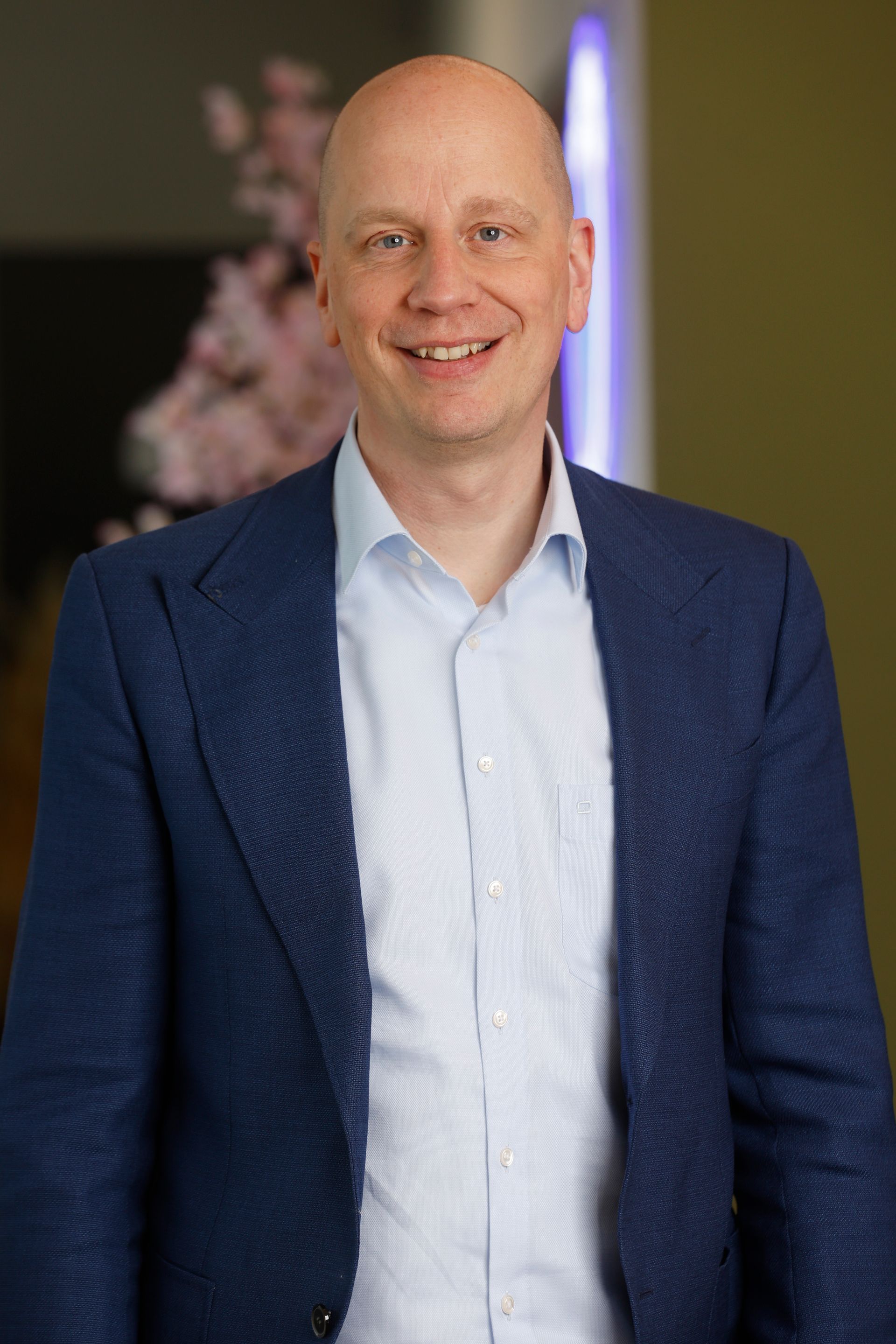 Een man in een blauw shirt lacht naar de camera.