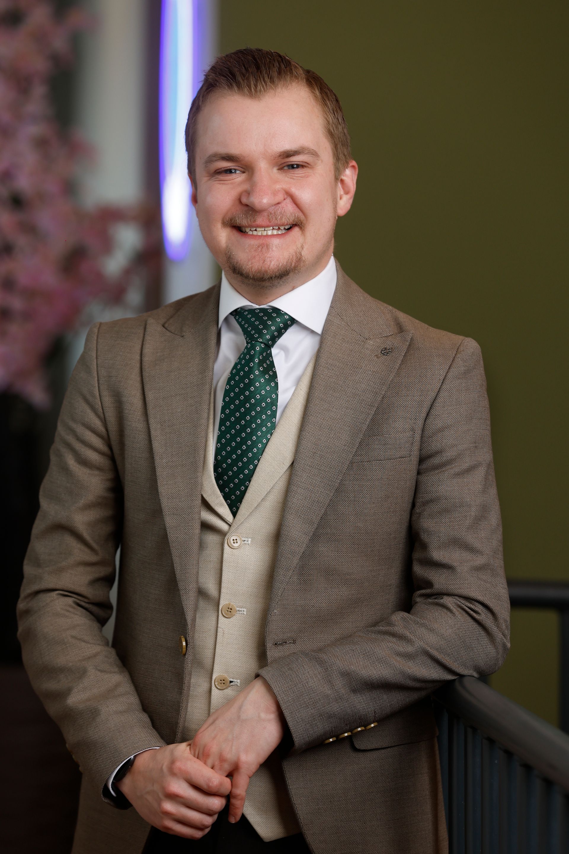 Een man in pak en stropdas lacht en heeft zijn armen over elkaar.