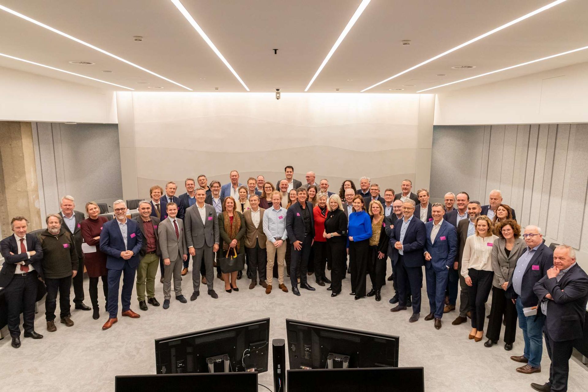 Een grote groep mensen poseert voor een foto in een vergaderzaal.