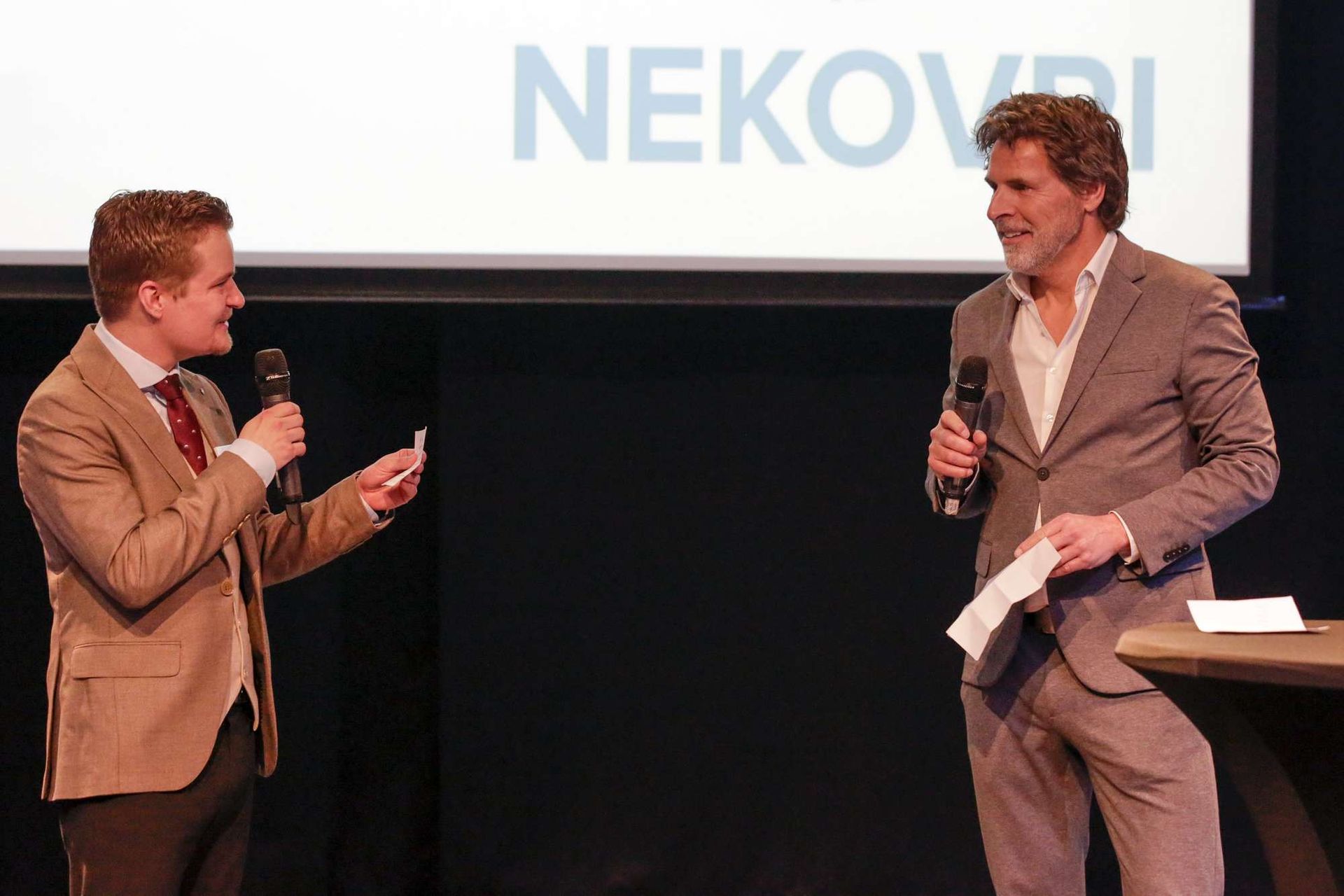 Twee mannen staan āāvoor een scherm waarop nekovri staat
