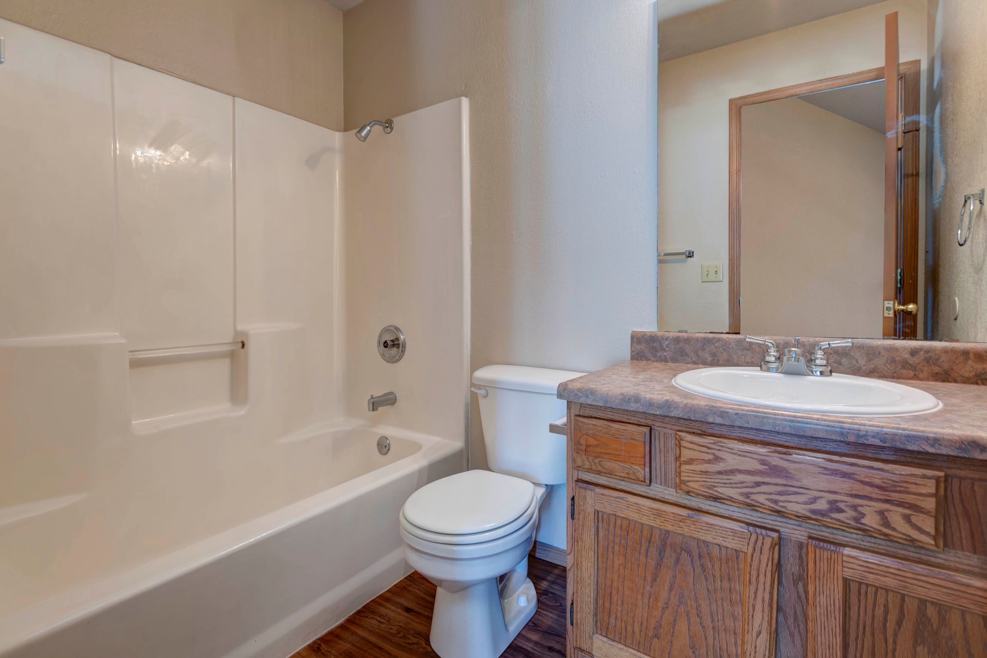 Photo of a shower/bathtub combo, next to a toilet, which is next to a wood cabinetry sink
