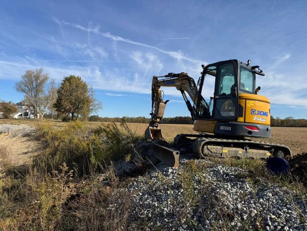 Yellow excavator working in a grassy wetland under a blue sky