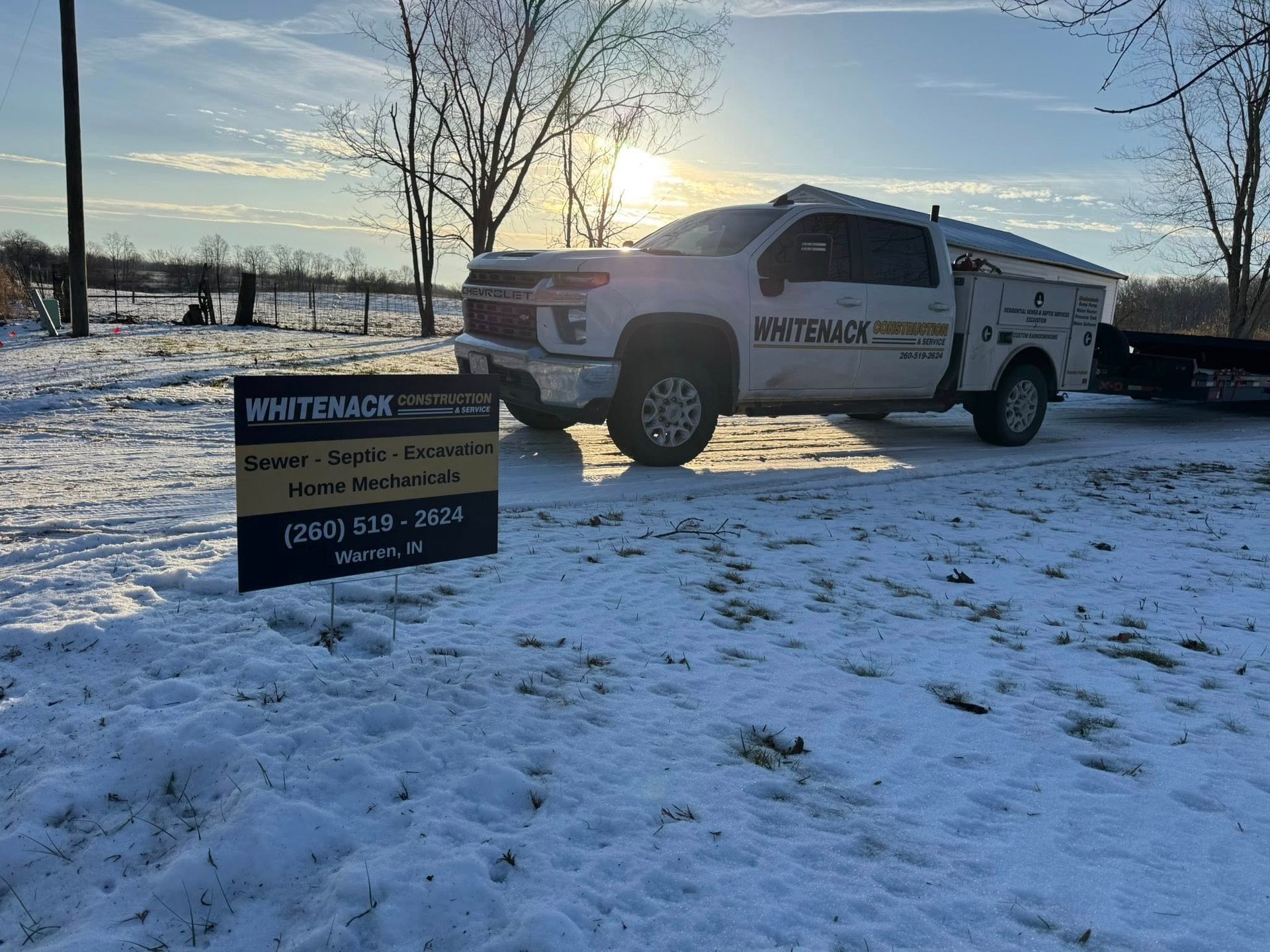 Truck parked in snowy field at sunset beside a real estate sign.