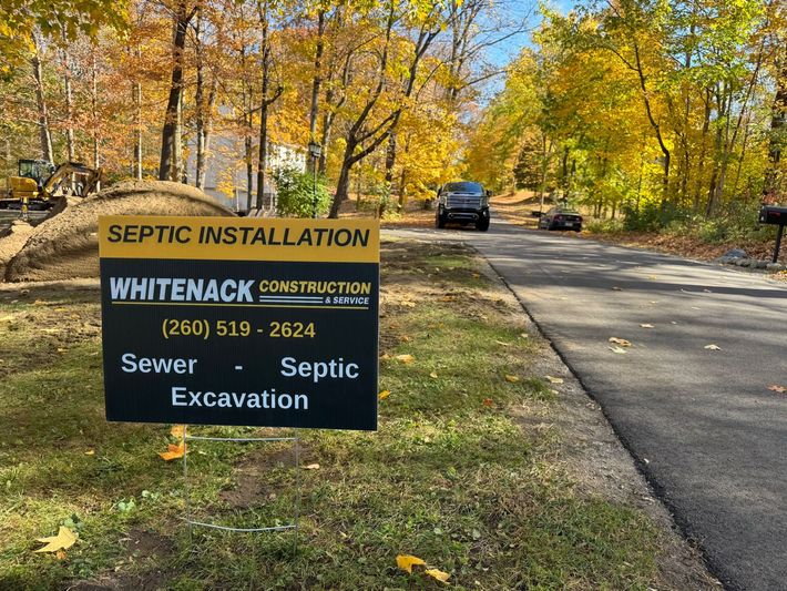 Yellow septic installation sign beside a road with autumn trees and a parked truck behind it