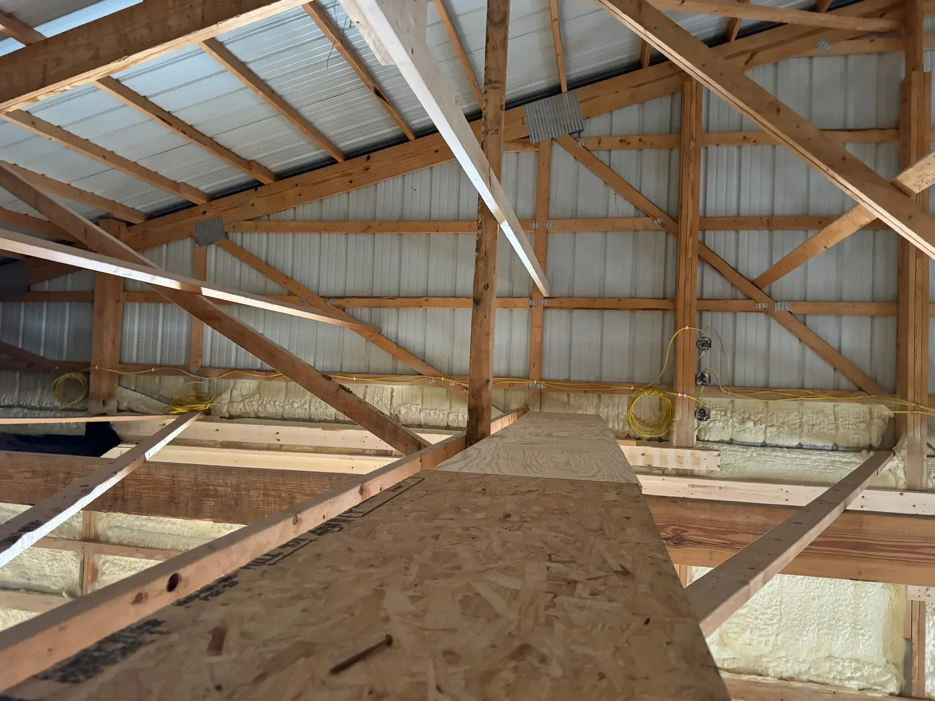 Interior of a wooden barn loft with exposed beams and plywood flooring under a metal roof
